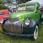 A green truck parked in the grass next to other cars.